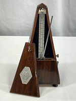 Front view of the metronome showing wooden casing and removable front panel with metallic plaque.