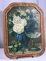 Full view of vintage framed print featuring white and dark roses in blue vase with decorative glass bowl on right, ornate wood and gold floral frame overall.
