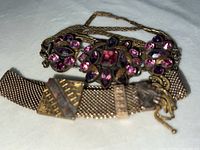Two antique Victorian style bracelets: one with flower-shaped purple and pink rhinestones and linked chain band, the other with metal mesh band and geometric clasp details.