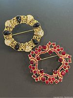 Both wreath brooches shown side by side on a black surface, displaying front and back of the pieces.