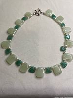 Full view of the green aventurine stone necklace laid out flat showing alternating rectangular light green and triangular darker green stones, interspersed with pearls and beads.