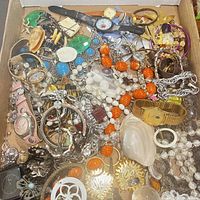 Full view of a box containing a mix of vintage jewelry items including watches, bracelets, earrings, and necklaces, showing condition and variety.