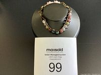 Front view of the bracelet displayed on a black stand with a maxsold auction label showing 99.