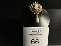Photo of the brooch displayed on a black stand with auction lot card in the background