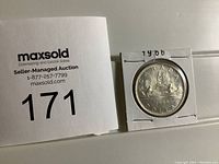 Photo showing the coin and auction lot number sign side by side for identification.