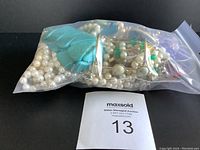 Bag of clear plastic containing various costume jewelry items including faux pearl necklaces and turquoise colored stone bracelets.