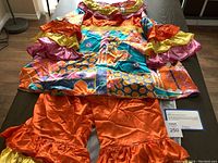 Full view of the colorful patchwork ruffled top with orange ruffled slacks laid flat on a table