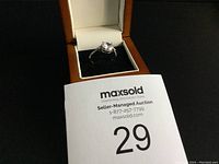 Full view of ring in orange and white ring box with auction number card