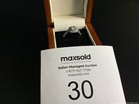 Ring displayed in a brown and white jewelry box on black velvet.