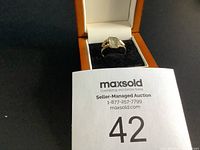 Estate ring in an open jewelry box with black velvet interior, showing the rectangular light green gemstone and gold-tone metal band with side motifs.