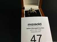 Ring displayed in an open box, showcasing the turtle design with blue and clear stones.