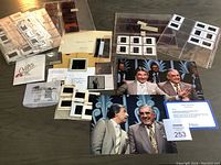 Multiple color and black-and-white photographic slides, slide holders, envelopes, and two printed photographs on table surface.