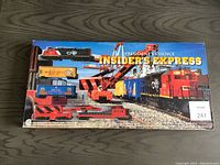 Box showing the full train set with locomotive, multiple freight cars, and crane car in a railway setting with tracks and containers.