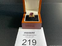 Front view of gold ring with purple stone in decorative setting inside velvet-lined wooden box
