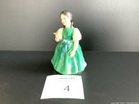 Royal Doulton Francine porcelain figurine showing young girl in green dress holding a bird, front view.