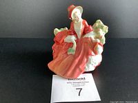 Front view of Lydia figurine showing seated woman in red dress holding a green book.