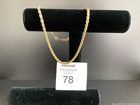 Gold plated rope chain necklace displayed on black jewelry stand with auction tag visible