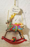 Front view of multi-colored rocking reindeer ornament with accompanying cloud sign stating 'Baby’s 1st Christmas'.