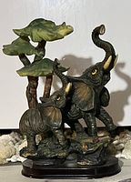 Photo showing a figurine with two elephants, green tree, and rock base against a neutral background.