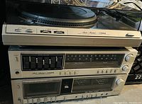 Photo showing the full Fisher system including turntable on top, graphic equalizer with sliders, and tuner unit with analog dial, power and tuning knobs.