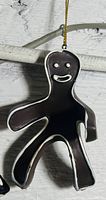 Photo of a dark brown gingerbread man shaped tree ornament with white icing outlines and gold hanging string.