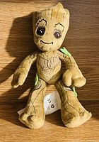 Front view of Groot plush toy showing detailed bark-like texture, embroidered eyes, and green leaf accents on limbs. Condition is good.