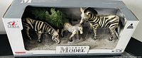 Three zebra figurines in original box packaging against a desert style background with bushes, labeled Series Model by brand Aolex.