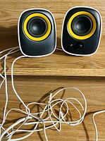 Front view of two Philips desktop speakers connected by white wires, each with black front and yellow ring around speaker cone, placed on a wooden shelf.