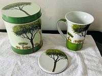 Photo showing the full set of safari-themed ceramic mug with lid and matching cylindrical canister with lid, displayed on white cloth.