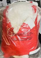 Photo of the Santa suit set containing a red jacket, Santa hat, and white beard packaged in clear plastic.