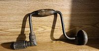 Photo of a vintage manual hand drill showing wooden handle and crank, metal chuck at end.