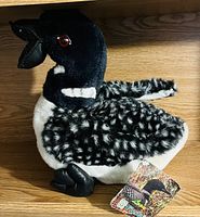 Plush loon toy with black and white body, red eyes, open beak, black feet, and original illustrated tag attached.
