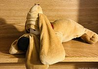 Photo of a vintage plush dog toy lying on its side, featuring long droopy ears, closed eyes, a large black nose, and a bandage wrapped around its head.
