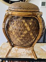 Front view of the large footed rice basket showing woven pattern and curved bamboo supports forming the stand under the basket, with matching woven lid.