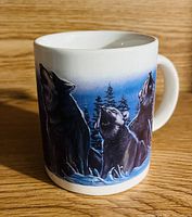 White ceramic mug with a print of three howling wolves against a snowy forest background at dusk.