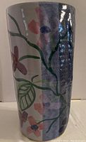 Side view of the cylindrical ceramic vase showing blue and pink flowers with green leaves, glossy finish.