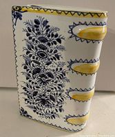 Front and side view of ceramic book bud vase showing floral design and structure