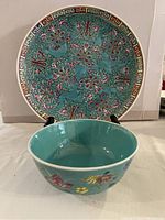 View of the bowl in front of the plate, showing turquoise color and floral designs on both pieces.