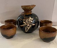 Front view of sake bottle with four cups arranged around it, showing glaze and character detail.