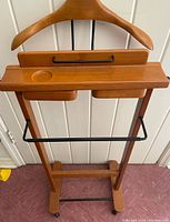 Front view of wooden butler's rack showing hanger, compartments, and black metal towel bar