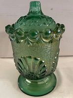 Close-up image of a green carnival glass candy jar with textured body, decorative rim, and matching lid on pedestal base.