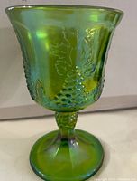 Photo of a green carnival glass goblet showing grape and leaf embossed pattern with iridescent finish.