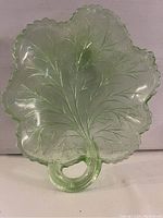 Front view of green carnival glass leaf-shaped dish with leaf vein and scalloped edge details. Ring-shaped handle is prominent.