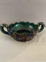 Front view of round carnival glass candy dish showing curved handles, detailed pressed patterns and scalloped rim.