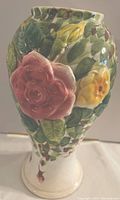 Front perspective view of ceramic vase with pink and yellow rose flowers surrounded by green leaves on textured ceramic surface.