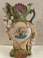 Front view of one porcelain cherub vase showing hand-painted flowers and two cherub figures on the sides and front.