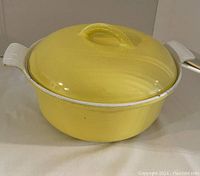 Yellow enameled cast iron Dutch oven with lid on a white surface.