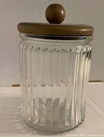 Front view of clear glass cigar holder with vertical ribbing and wooden lid on top.