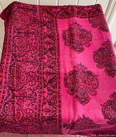Photo of folded rectangular tablecloth with pink fabric and black Indian print pattern laid out on a door.