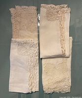 Four folded cloth napkins with intricate lace edges in cream and beige colors laid flat for display.